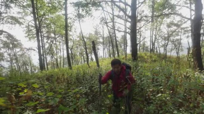 穿着红色衬衫背包划桨的高级老人拿着登山杖在山上爬坡