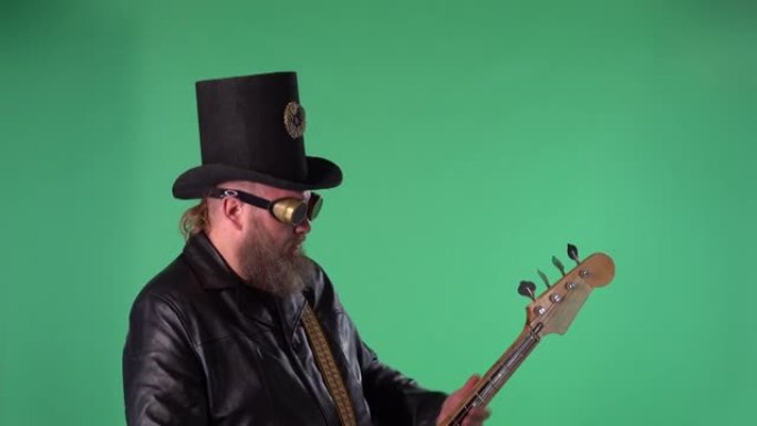 留着胡须的男人穿着长皮大衣，戴着爱尔兰风格的帽子，戴着原始眼镜，弹奏红色吉他。摇滚音乐家在工作室的绿