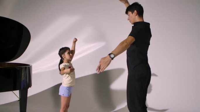 小女孩的个人芭蕾舞课。专业老师向女孩教授舞蹈元素，并纠正手的位置。勤奋的芭蕾舞学生在白色工作室背景下
