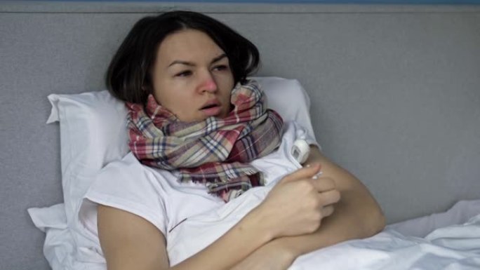 生病的年轻女子躺在床上测量温度。她咳嗽，发冷，流鼻涕。流感、感冒或冠状病毒症状