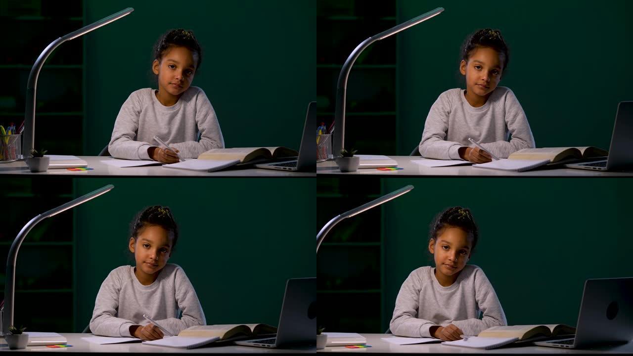 女孩若有所思地看着镜头，从手中松开了笔。一个女孩在夜灯的灯光下坐在桌子旁做作业。特写。慢动作就绪59
