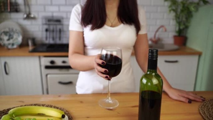无法辨认的女人的特写镜头在厨房里摇一杯红酒。不知名的女性用酒精摇动酒杯。慢动作