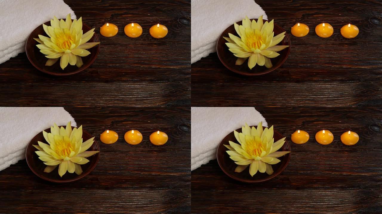 木桌上的黄莲睡莲花、毛巾和燃烧的蜡烛