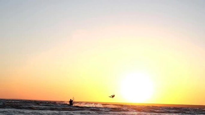 风筝冲浪者在夏天的日落下在水上飞行时做了一个技巧，慢动作