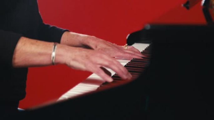 一个成年白人妇女的手在红色工作室背景前在钢琴上演奏长时间的和弦的特写静态镜头