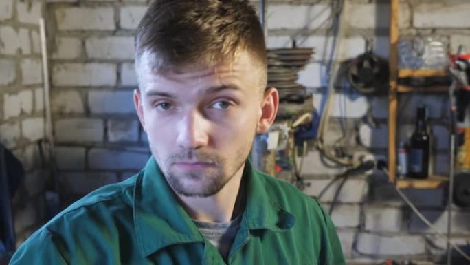 工作服专业机械师脱下防护眼镜，擦去额头上的汗水。疲惫的年轻修理工在车库里看着相机的肖像。维护服务理念