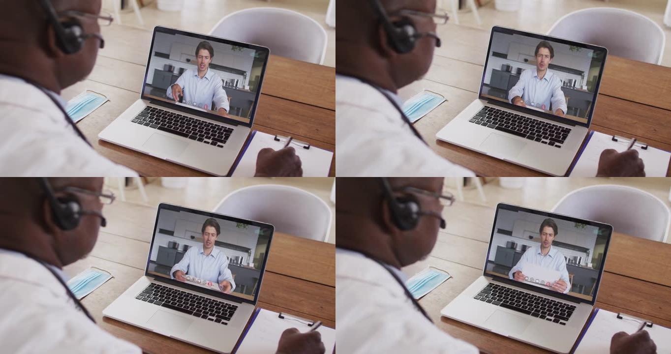 非裔美国男性医生戴着电话耳机在笔记本电脑上进行视频通话时做笔记