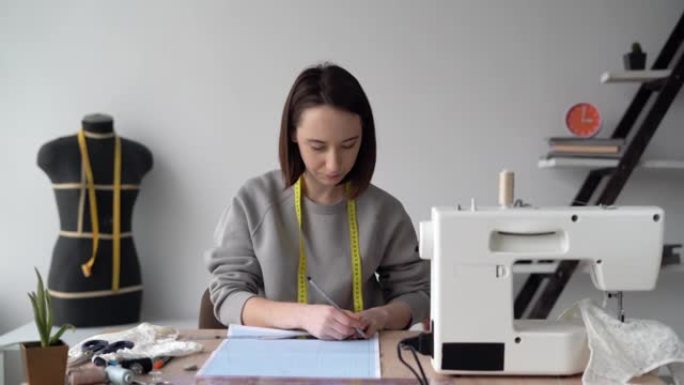 年轻的高加索女孩设计师内衣坐在桌旁，在方格纸上画画。创建一个新的衣服集合。小企业概念。复制空间。文本