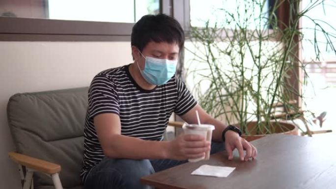 戴着口罩的亚洲男子在咖啡店喝咖啡。