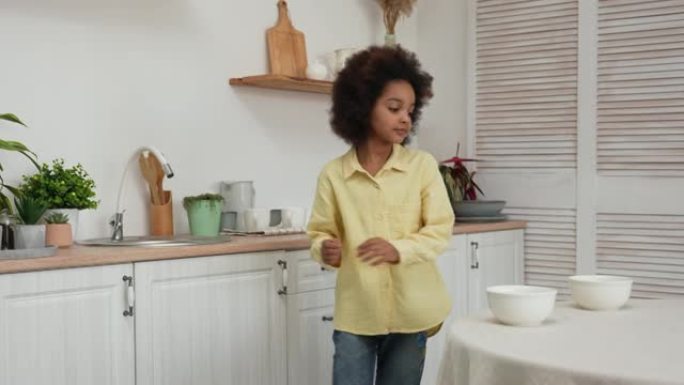 小非洲裔美国女孩从桌子上取下深白色的碗，然后将它们放在水槽中清洗。饭后。十几岁的女孩在明亮的厨房背景