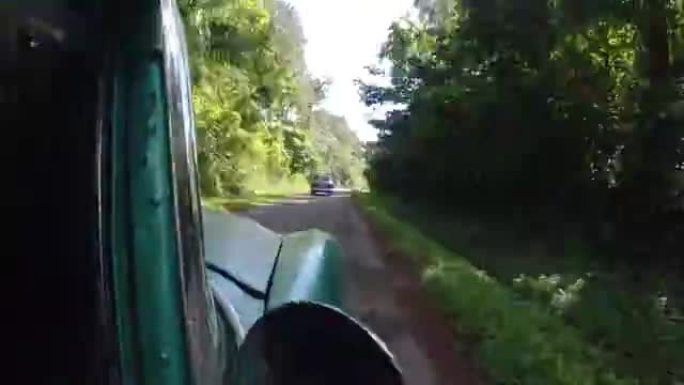 在阳光明媚的夏天，绿色的老式汽车在乡村道路上行驶。