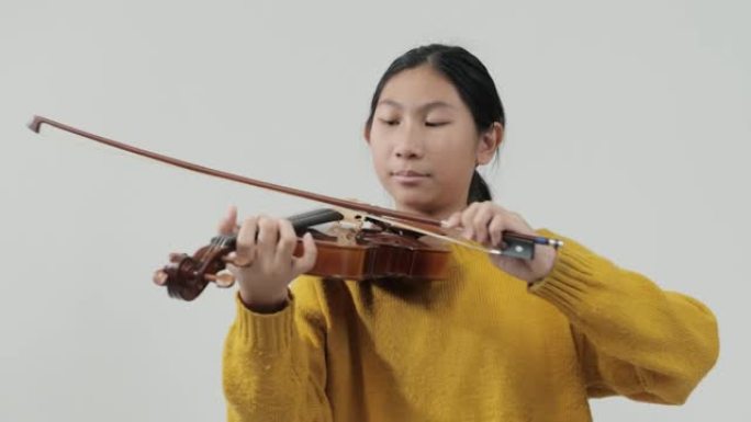 穿着黄色毛衣的亚洲女学生学习小提琴与灰色背景，生活方式概念。