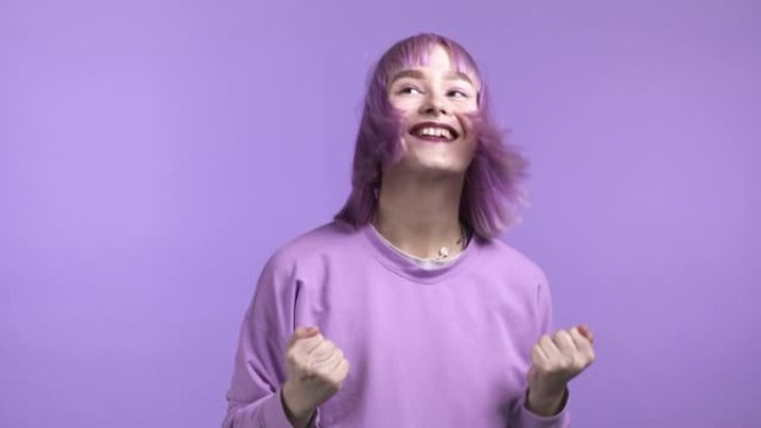 染成紫色头发的女人非常高兴和快乐，她表现出胜利的姿态，她实现了结果，目标。紫罗兰工作室背景上惊讶兴奋