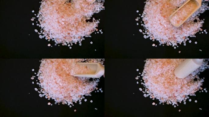粉色喜马拉雅盐。黑色背景上木勺中的喜马拉雅粉色岩盐。粉色喜马拉雅盐细粒