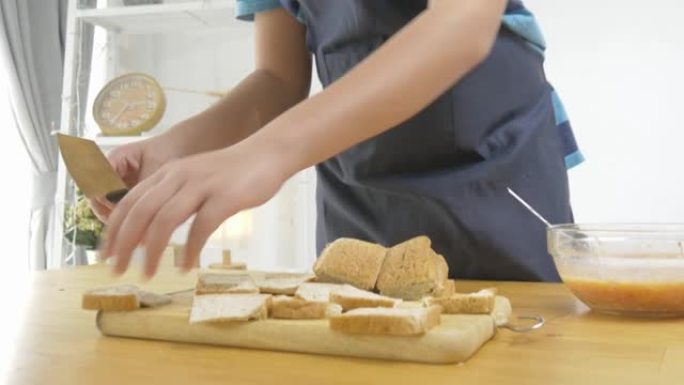 亚洲男孩穿着蓝色围裙，在烹饪前将猪肉和鸡蛋混合在迷你面包上，准备食物概念。