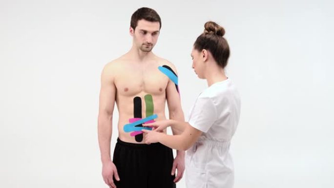 女性治疗师在男人的腹部应用运动学胶带。女人准备男性患者将kinesio胶带粘在腹部或腹部