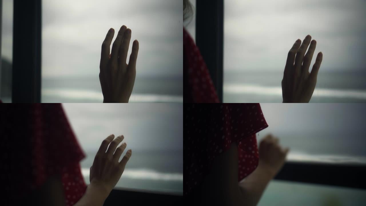 欧洲女孩站在窗户后面的房子里，用手触摸红色连衣裙上的木框