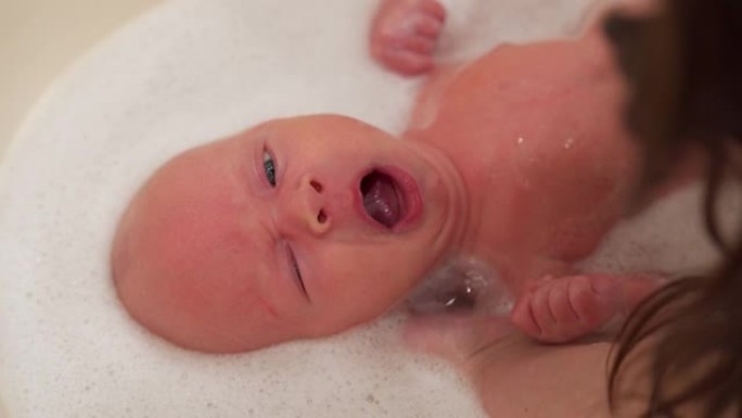 母亲在婴儿洗澡时给新生男婴洗澡，面对1个月大的新生男婴特写镜头。