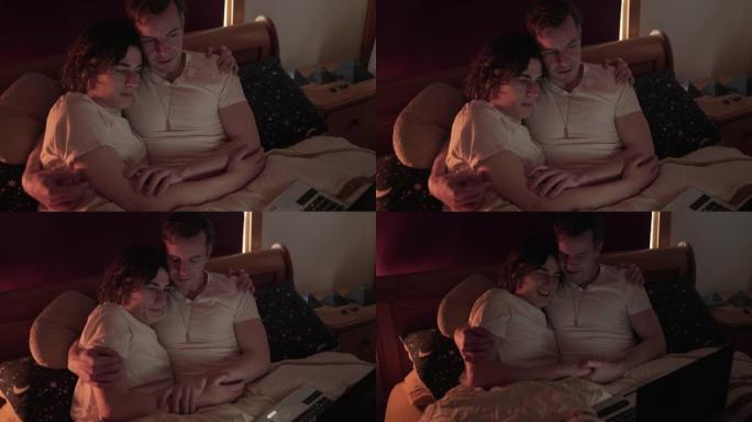 一对年轻夫妇坐在床上一起在笔记本电脑上看电影