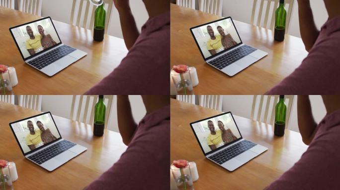 混合种族男子坐在桌子旁，使用笔记本电脑与朋友进行视频通话