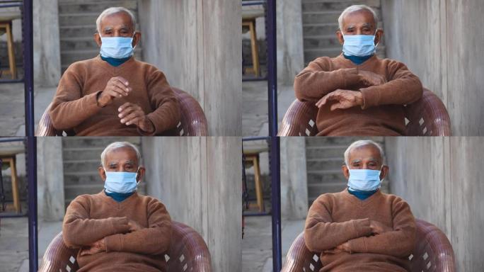 在电晕病毒大流行期间戴着防护口罩，双手交叉坐在家里的印度老人肖像