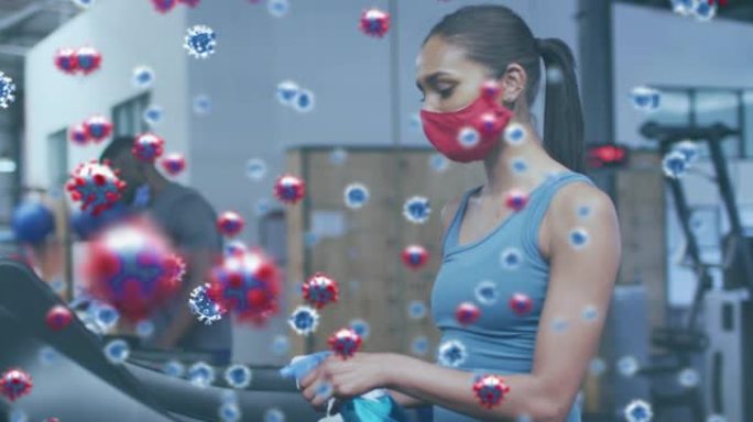 新型冠状病毒肺炎细胞漂浮在戴着口罩的女人身上，用消毒剂清洁健身器材