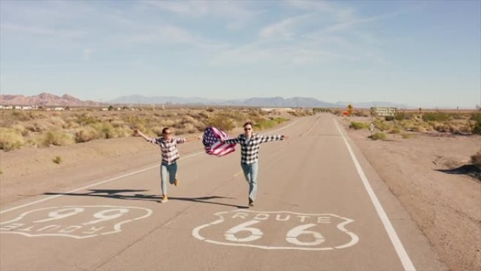 年轻夫妇举着美国国旗，在空旷的路上奔跑。