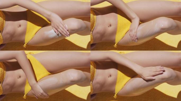 穿着泳衣躺在毯子上的适合女人在大腿上涂抹防晒霜