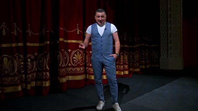 穿着西装的男人站在舞台上用麦克风开玩笑。有趣的表演。幽默的喜剧演员向观众讲话。