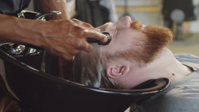 理发师从男人的头发上冲洗洗发水