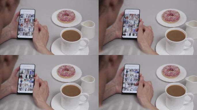 在家中的女人坐在餐桌旁喝咖啡和甜甜圈，使用智能手机滚动浏览帐户提要。女孩在手机上看社交网络页面。女人