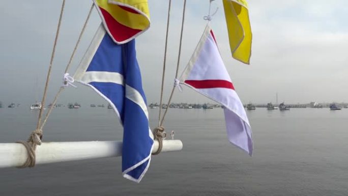 桅杆上的航海信号旗，背景是港口中的锚定船。