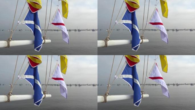 桅杆上的航海信号旗，背景是港口中的锚定船。