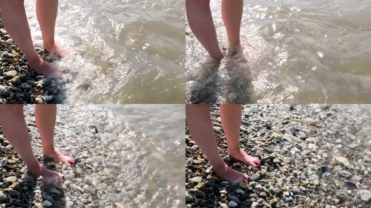 鹅卵石滩上有明亮黑色修脚的女性腿被海浪冲刷。概念。暑假概念，女人的脚在温暖的海水和泡沫，鹅卵石海滩，