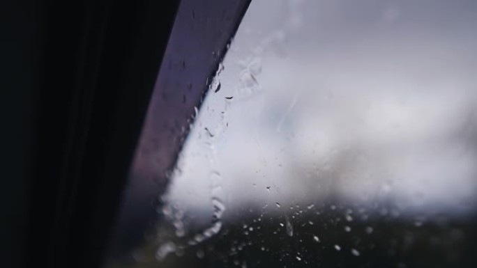 在雨中行驶时，水滴沿着车窗向下流过。特写拍摄