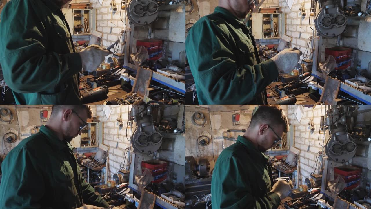 防护眼镜的年轻修理工在车库使用工具检查车辆细节。专业修理工在工作场所工作。穿着制服的男机械师在车间工