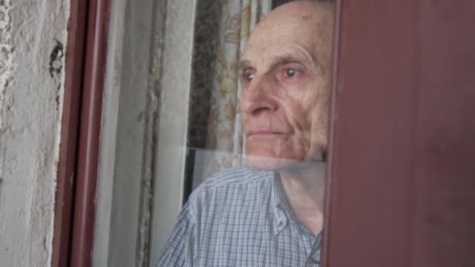 悲伤的老人站在门玻璃后面，透过窗户看。