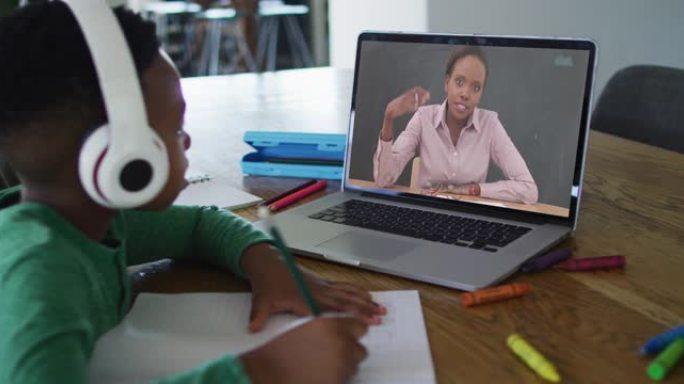 非裔美国男孩在家里做作业时戴着耳机在笔记本电脑上进行视频通话