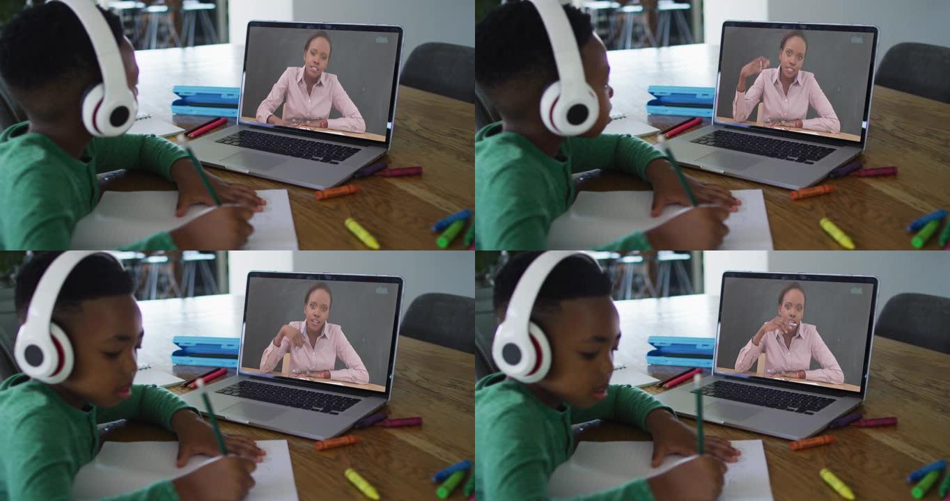 非裔美国男孩在家里做作业时戴着耳机在笔记本电脑上进行视频通话