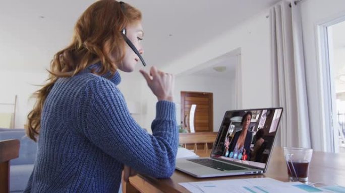 戴着电话耳机的白人妇女在家里的笔记本电脑上与女同事进行视频通话