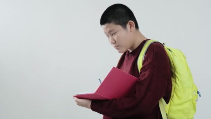 快乐的亚洲男生穿着红色毛衣在灰色背景，生活方式概念上的粉红色书讲座。