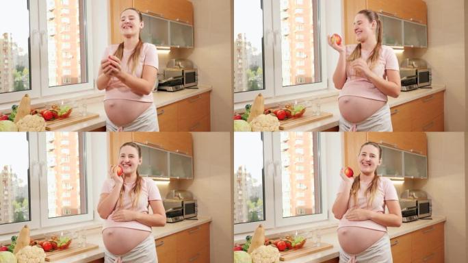 快乐微笑的孕妇在吃早餐时在厨房扔和抓红色成熟的苹果。怀孕期间健康生活方式、营养和水合的概念