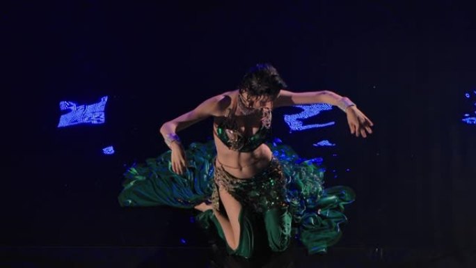 一个潮湿的东方女人坐在水面上跳着肚皮舞的俯视图。一位穿着传统服装的黑色长发的异国情调的舞者在黑暗的工