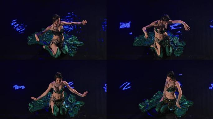 一个潮湿的东方女人坐在水面上跳着肚皮舞的俯视图。一位穿着传统服装的黑色长发的异国情调的舞者在黑暗的工