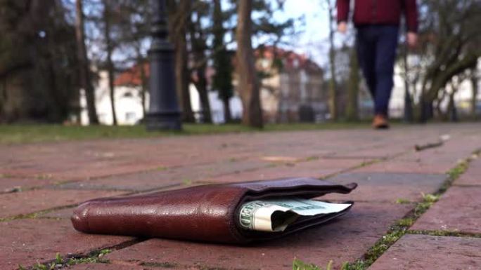 白人男性捡起一个丢失的棕色皮革钱包，放在城市公园的地上，里面有Monney Bill