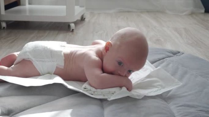 婴儿的肚子时间，婴儿学习头部控制，3个月大的男婴抬起头躺在肚子上活动在家里玩垫子。
