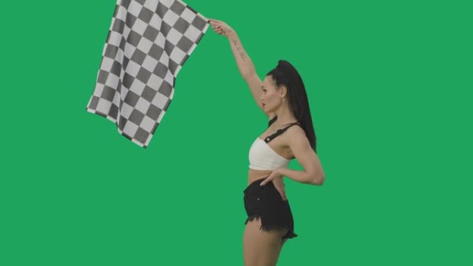 黑发挥舞着黑白方格赛车旗的侧视图，标志着比赛开始。年轻女子在绿屏背景下摆姿势特写。慢动作就绪，4k，