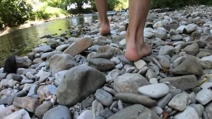 赤脚走在河岸上的年轻人的慢动作跟踪镜头