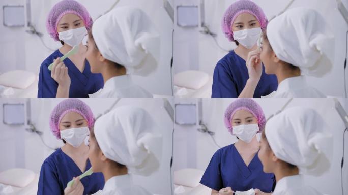 戴着卫生发帽的医务人员的微笑为在白色医疗沙发上穿着浴袍的年轻亚洲妇女提供面部护理服务