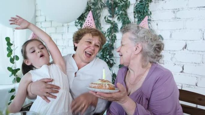 三个女人一代庆祝高级女人85岁生日，奶奶拿着蛋糕和快乐一起吹蜡烛。女性家庭享受、尊重和温暖的关系。庆